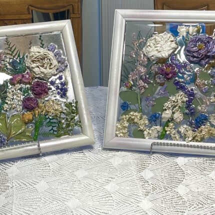 Two framed pictures of flowers are sitting on a table.